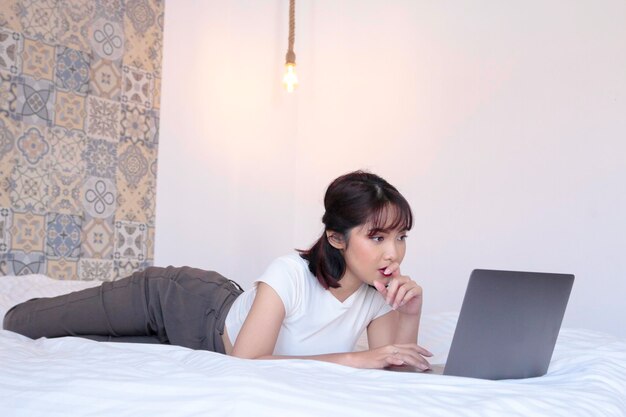 Linda garota asiática séria trabalha o laptop na cama Trabalha em casa conceito