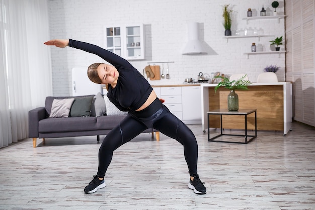 Linda garota atlética em uma legging e um top faz exercícios de alongamento. Estilo de vida saudável. A mulher pratica esportes em casa.