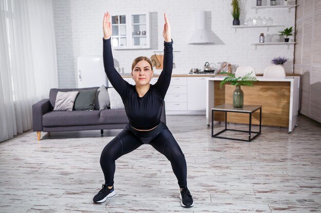 Linda garota atlética em uma legging e um top faz exercícios de alongamento. estilo de vida saudável. a mulher pratica esportes em casa.