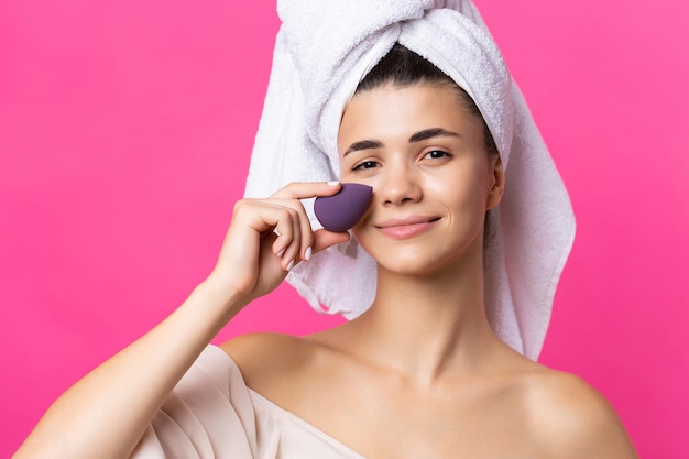 Foto linda garota atraente alegre com uma toalha na cabeça dela segura uma esponja contra um fundo rosa