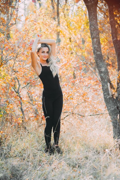 Linda garota atraente posando na floresta de outono em calças pretas e uma camiseta com um lindo cabelo branco fofo