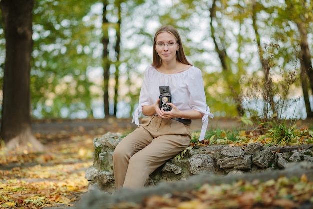 Linda garota atraente segurando uma câmera de reflexão de lente dupla vintage retrô no parque outono