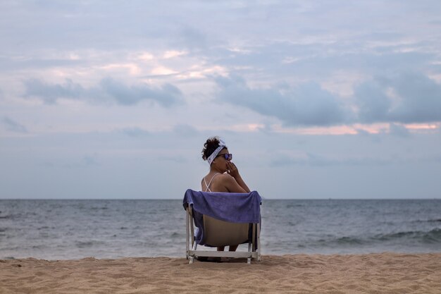 Linda garota bocejando em uma espreguiçadeira na praia perto do oceano em tempo nublado. conceito de férias.