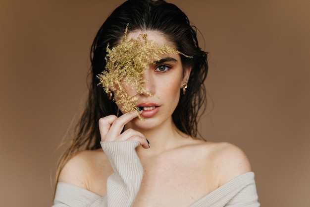 Linda garota branca posando com interesse com a planta deslumbrante morena em pé sobre fundo marrom