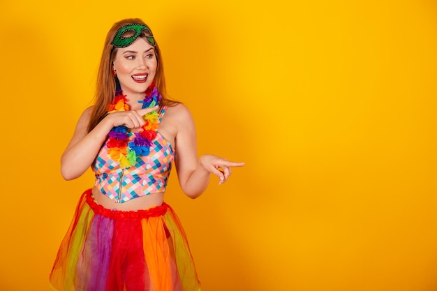 Linda garota brasileira ruiva em roupas de carnaval apresentando algo à direita