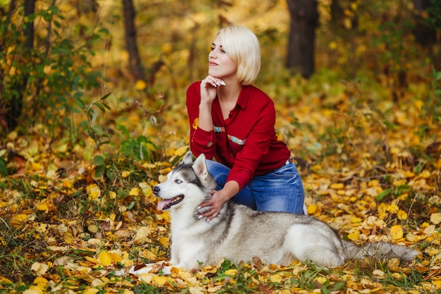 Linda garota caucasiana brinca com cachorro husky na floresta de outono ou parque