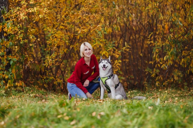 Linda garota caucasiana brinca com cachorro husky na floresta de outono ou parque