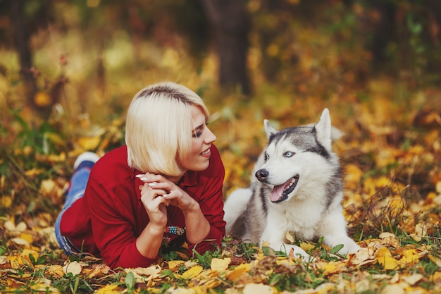 Linda garota caucasiana brinca com cão husky na floresta de outono