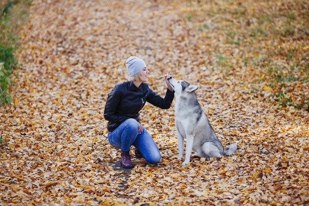 Linda garota caucasiana brinca com cão husky na floresta de outono