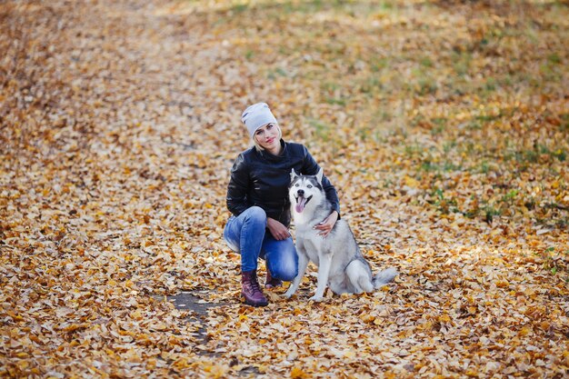 Linda garota caucasiana brinca com cão husky na floresta de outono