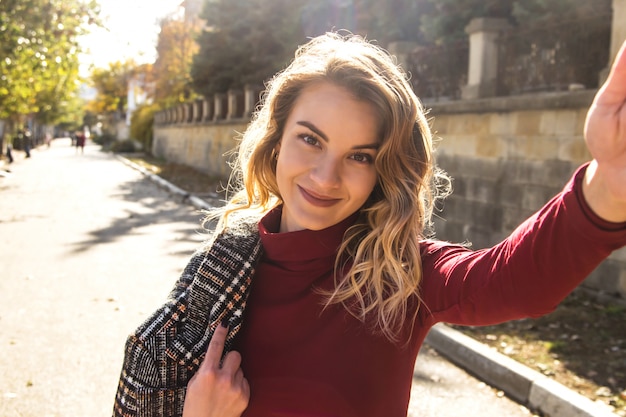 Linda garota caucasiana tira uma selfie na cidade de outono e sorri.