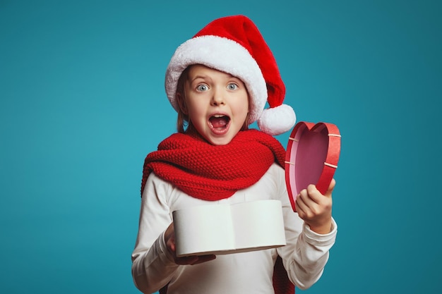 Linda garota chocada com chapéu de Natal segurando uma caixa de presente aberta