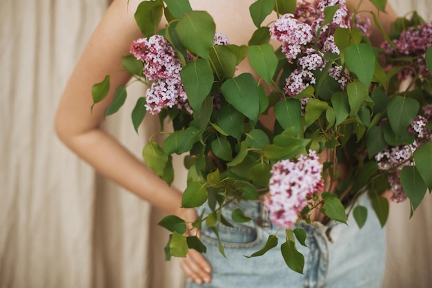 Linda garota cobrindo a parte superior do corpo nua com flores lilás florescendo Imagem criativa de ternura e sensualidade Jovem com crescimento de jeans lilás ramos lilás vista recortada