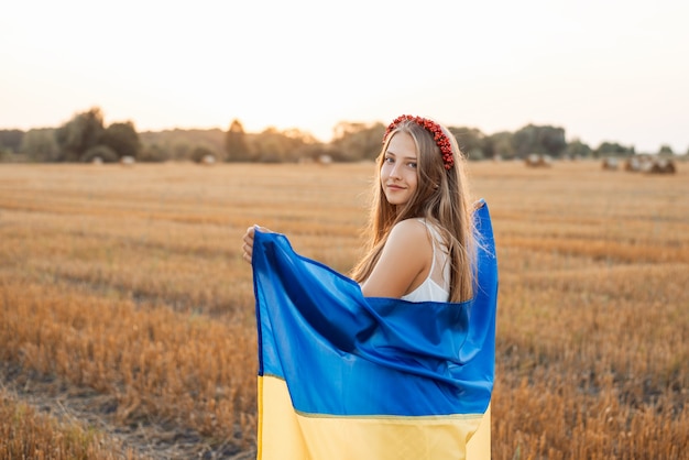 Linda garota com bandeira ucraniana em um campo de campo contra o sol poente