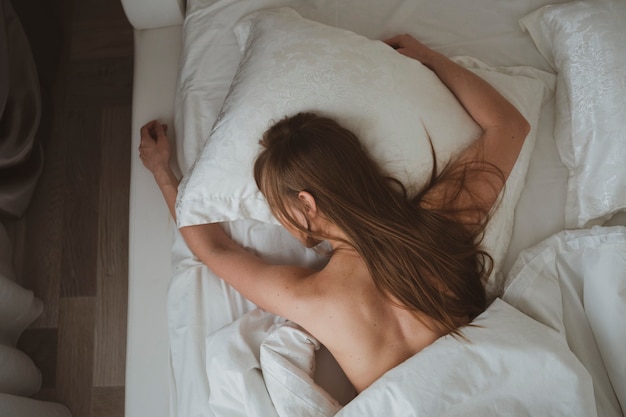 Linda garota com cabelo comprido dormindo em sua cama em lençóis brancos
