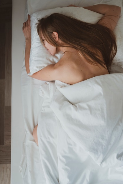 Linda garota com cabelo comprido dormindo em sua cama em lençóis brancos