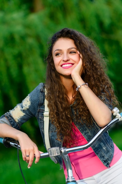 Linda garota com cabelo encaracolado andando de bicicleta no parque no verão na cidade