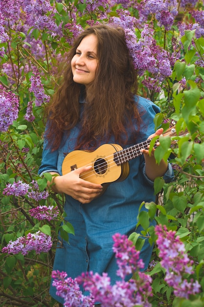 Linda garota com cabelo encaracolado vestida em jeans vestido tocando o ukulele