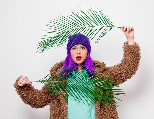 Linda garota com cabelo roxo na jaqueta com folha de palmeira.