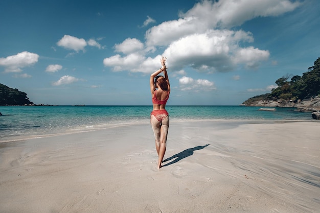 Linda garota com cabelo vermelho em pé e posando na praia perto do oceano. mulher caucasiana em maiô vermelho na costa. conceito de viagens. phuket. tailândia. vista traseira