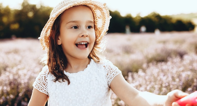 Linda garota com chapéu andando e sorrindo em um campo de lavanda em um dia ensolarado