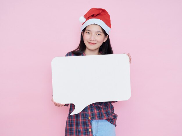 Linda garota com chapéu de Papai Noel segurando um pôster branco em branco sobre fundo rosa