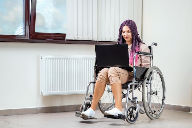 Linda garota com deficiência moderna trabalhando em um laptop em uma cadeira de rodas Trabalho em casa para o trabalho remoto freelancer deficiente