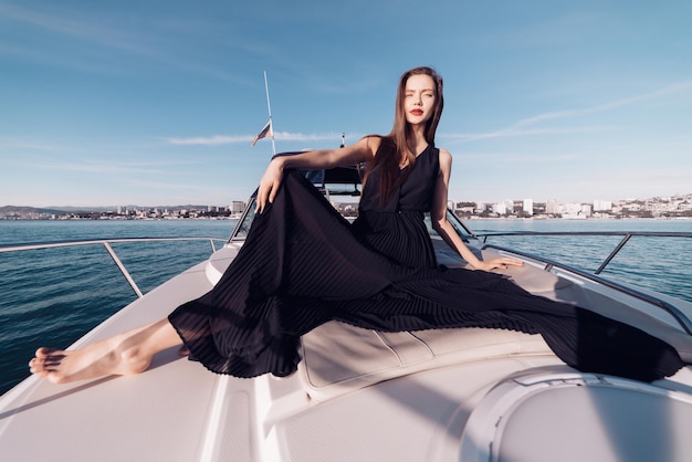 Foto linda garota com elegantes roupas de verão preto, descansando em seu iate branco, aproveitando as férias no mar