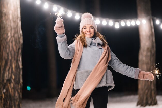 Linda garota com estrelinhas nas mãos Feliz inverno na floresta Luzes festivas de guirlanda