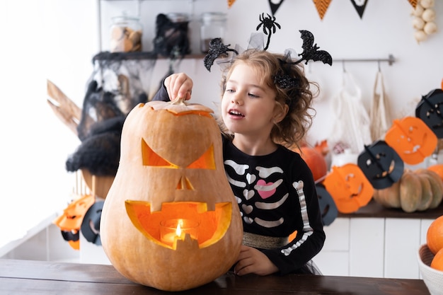 Linda garota com fantasia de bruxa com abóbora em casa na cozinha, se divertindo, comemorando o Halloween.