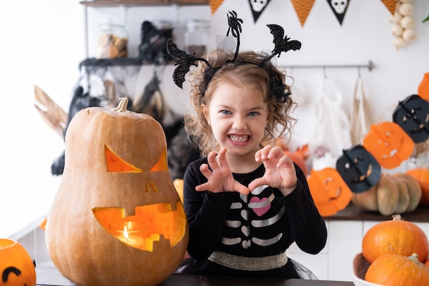 Linda garota com fantasia de bruxa com abóbora em casa na cozinha, se divertindo, comemorando o Halloween.