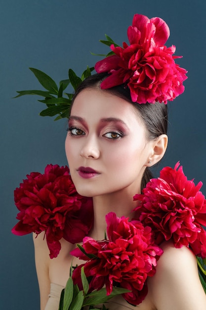 Linda garota com flores peônias nas mãos sobre um fundo azul Alegre modelo feminino posando no estúdio com buquê de flores da primavera