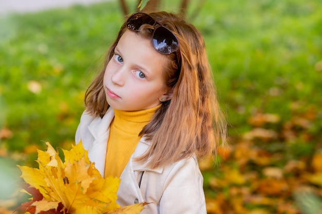 Linda garota com folhas de outono no parque de beleza. Menina de 8 anos em um parque de outono tem um buquê de folhas de plátano nas mãos. tempo ensolarado