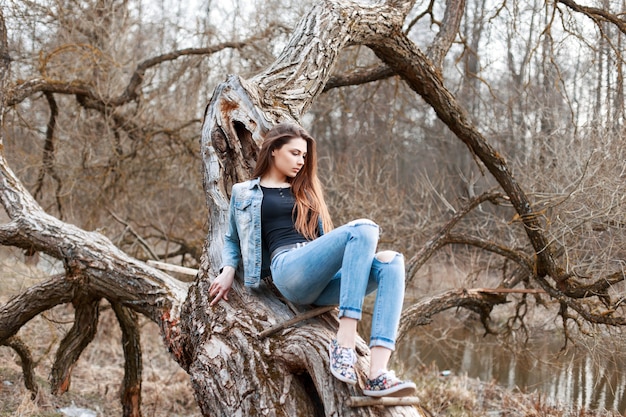 Linda garota com jaqueta jeans e shorts jeans sentada em uma árvore