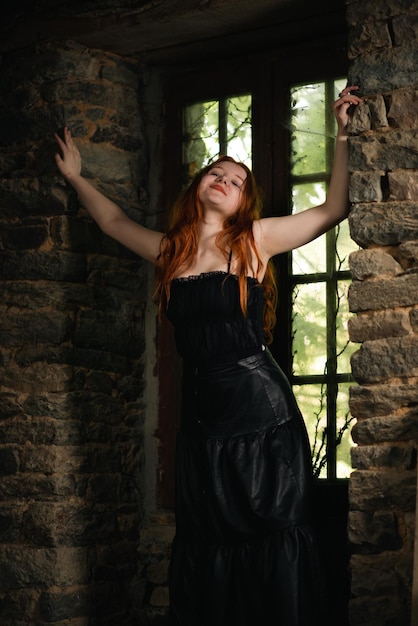 Linda garota com longos cabelos ruivos em um vestido preto em um quarto escuro