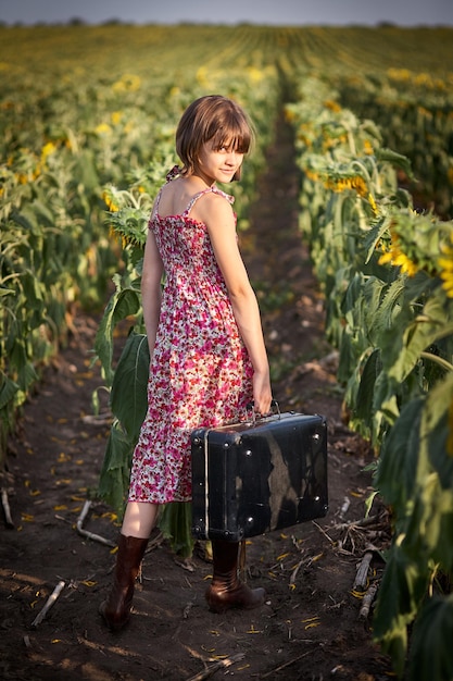 Linda garota com mala velha em um campo de girassol