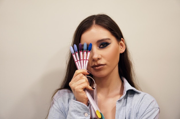 Linda garota com maquiagem azul cobre o rosto com uma paleta de unhas para manicure
