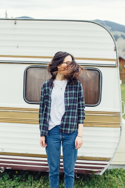 Foto linda garota com mochila viajando garota de pé perto de trailer viajando nas montanhas mulher de óculos viajando de carro garota viajante polegares para cima