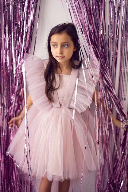 Linda garota com olhos grandes em um vestido rosa em contraste com o fundo de enfeites de ano novo