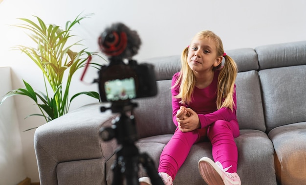 Linda garota com roupa casual rosa sorrindo para a câmera e falando sobre filmagem de vídeo com tecnologia. influenciador de mídia social infantil ou conceito de criador de conteúdo jovem em estilo casual relaxante em casa.