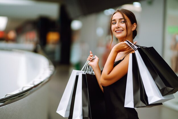 Foto linda garota com sacolas de compras, olhando para a câmera e sorrindo enquanto fazia compras no shopping