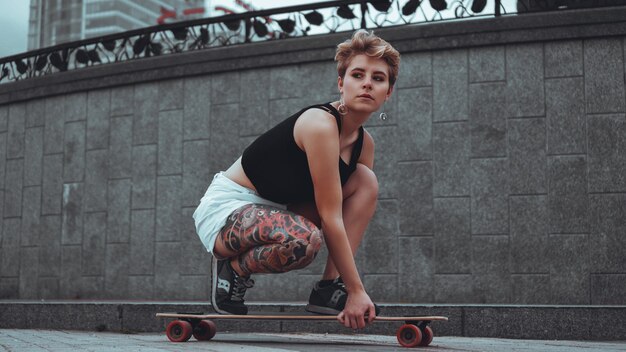 Linda garota com tatuagens senta-se no longboard. Ela tem tatuagem tradicional japonesa