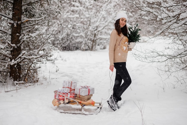 Linda garota com trenós, árvore de natal e presentes no inverno em um bosque nevado