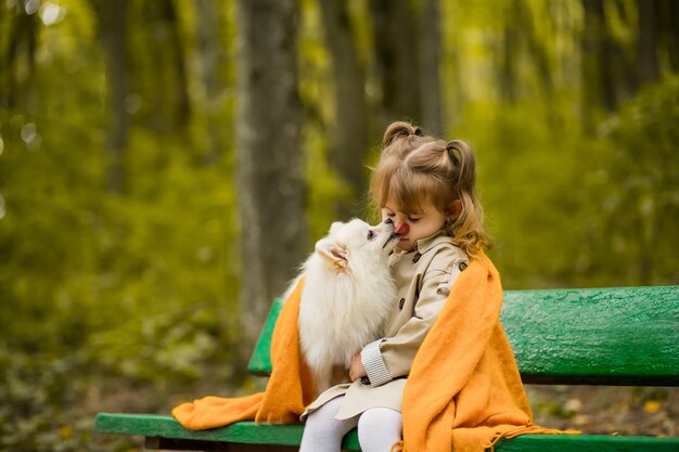 Linda garota com um cachorro está sentada em um banco no parque