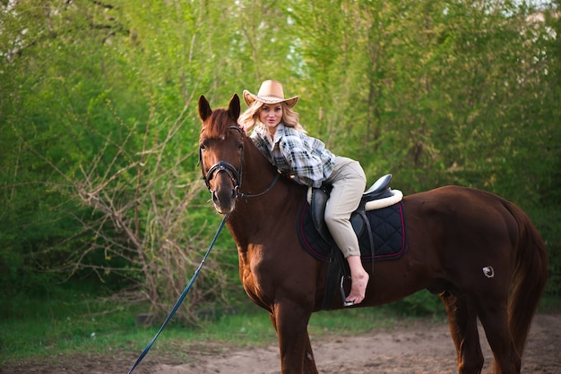 Linda garota com um chapéu, andando a cavalo no campo