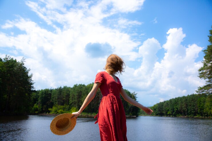 Foto linda garota com um chapéu de palha perto do lago. natureza incrível de verão. conceito de viagens. inspiração para o desejo por viagens. mulher de vestido de linho vermelho. materiais ecológicos para roupas.