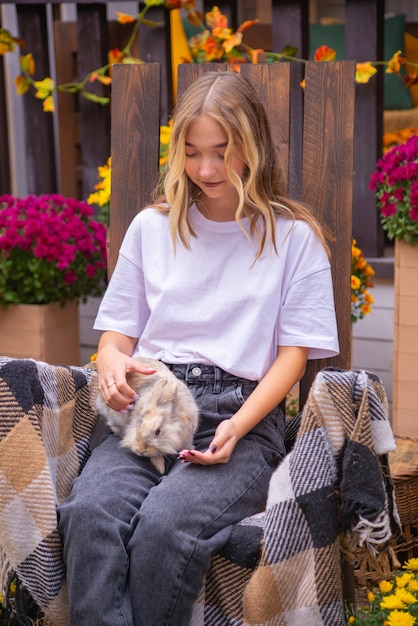 Foto linda garota com um coelho ao ar livre no outono perto da casa no banco