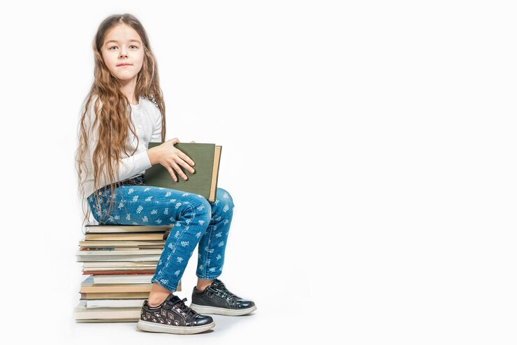 Foto linda garota com um livro sentado em uma pilha de livros sobre um fundo branco isolado