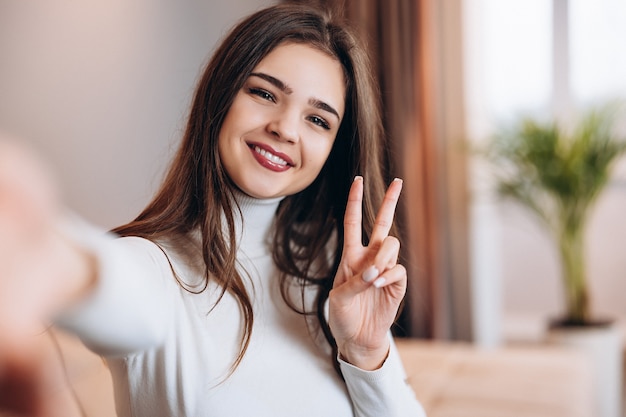 Linda garota com um sorriso lindo tirando uma selfie em casa