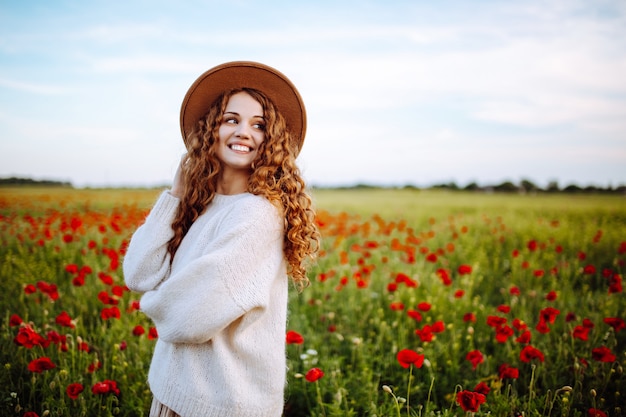 Linda garota com um suéter branco em um campo de papoulas